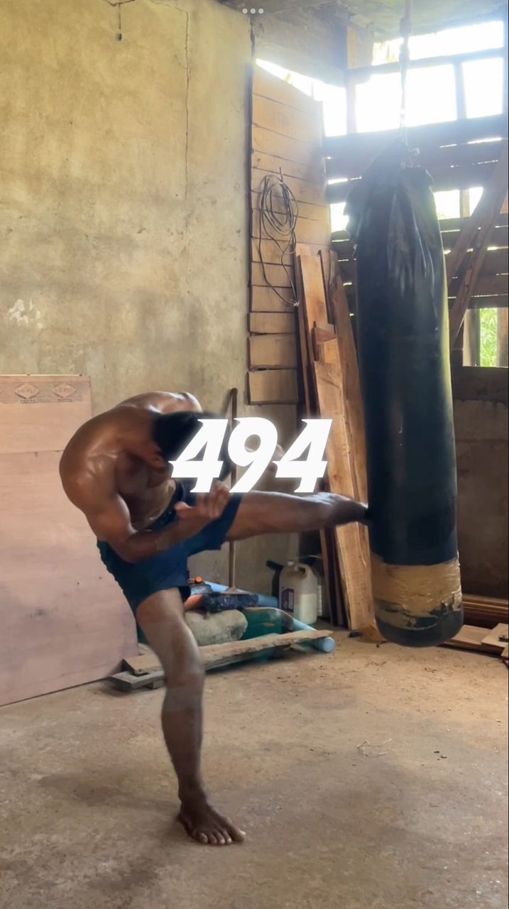 Muay Thai kick on a heavy bag in a bare concrete shed